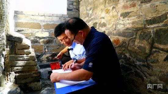 张景龙（左一）与同事利用仪器对丹崖山岩体进行监测（央广网记者 唐磊 摄）